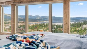 Een slaapkamer met een groot raam met uitzicht op een meer en bergen.