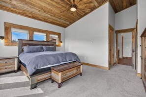 A bedroom with a large bed, wooden headboard, a nightstand, a bench, and a ceiling fan.