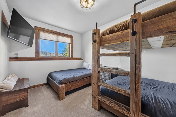 A room with bunk beds, a television mounted on the wall, and a window with a view of the outdoors.