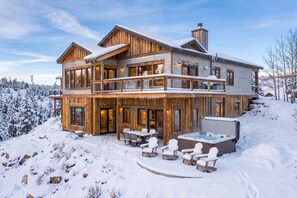 A two-story wooden cabin with a balcony, a hot tub, and a dining area.