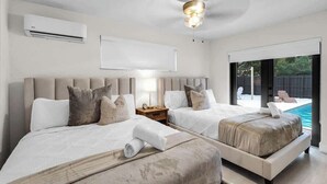 Una habitació d'hotel moderna amb dos llits, un ventilador de sostre, un aire condicionat, una taula de nit amb una làmpada i vista a una piscina.