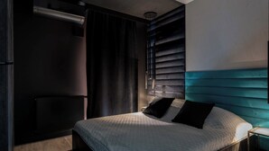 A modern bedroom with a large bed, dark walls, and a teal accent wall. - AS HOME Niegaleria (Wrocław)