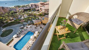 Ein Balkon mit Blick auf ein Schwimmbecken, Liegestühle und ein Tisch mit Getränken.