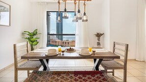 Ein Essbereich mit Holztisch, gedeckt für zwei Personen, mit Blick auf hohe Gebäude und einer hängenden Leuchte.