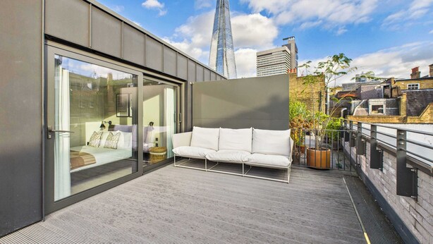 A modern rooftop terrace with a sofa, a glass door, and a view of the city skyline. - Edgy & Modern Balcony Apartment by Borough Market (Greater London)