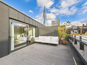 A modern rooftop terrace with a sofa, a glass door, and a view of the city skyline. - Edgy & Modern Balcony Apartment by Borough Market (Greater London)