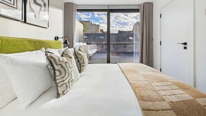 A modern hotel room with a bed, a view of the cityscape through large windows, and a balcony. - Edgy & Modern Balcony Apartment by Borough Market (Greater London)