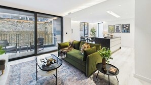 A modern living room with a green sofa, a glass coffee table, and a dining area in the background. - Edgy & Modern Balcony Apartment by Borough Market (Greater London)