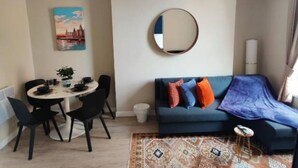 Een woonkamer met een ronde spiegel, een bank met kussens, een eettafel met stoelen en een kamerkleed met een patroon.