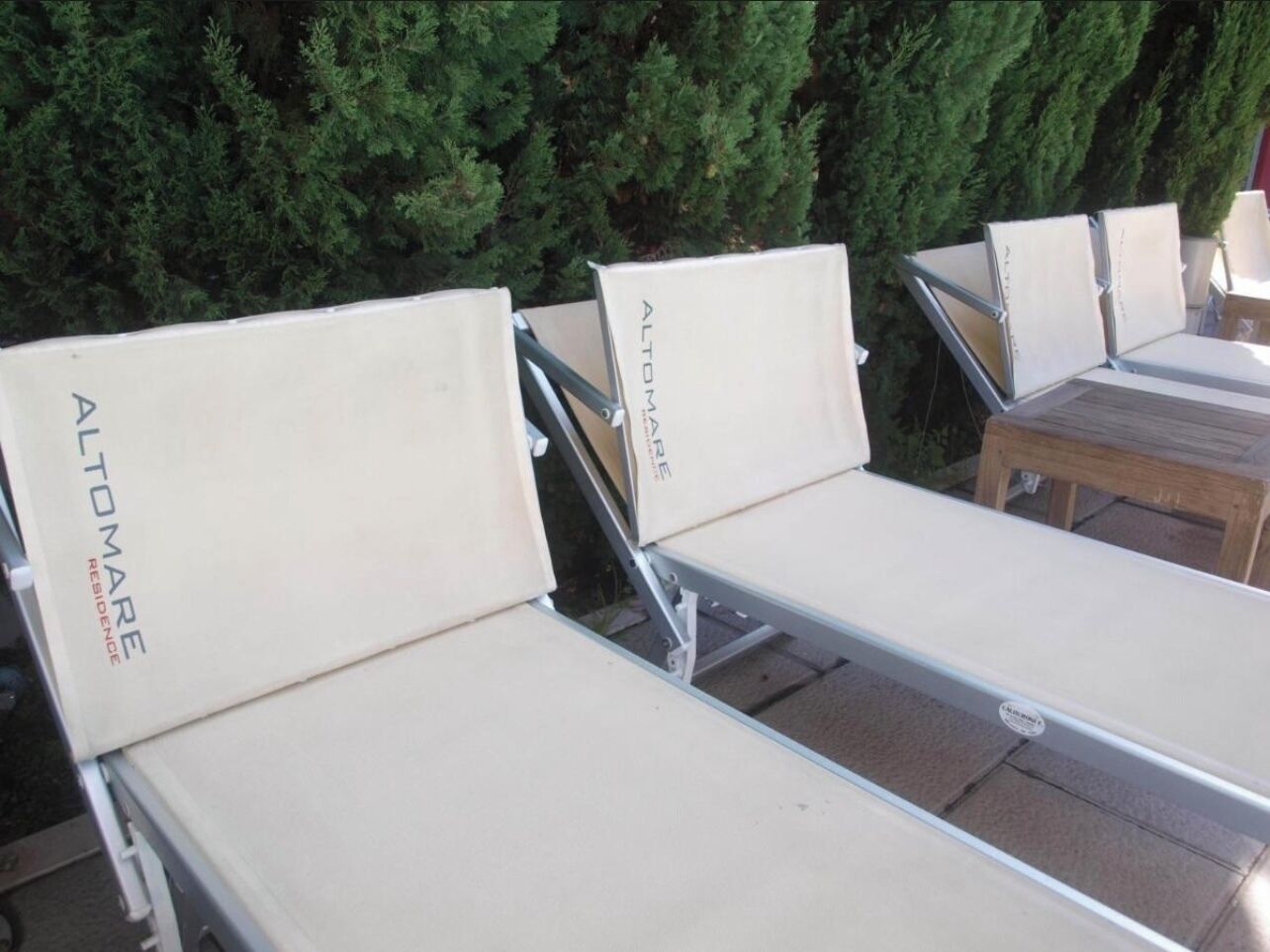 Outdoor lounge chairs with 'ALTOMARE RESIDENCE' branding, arranged in a row with a wooden table to the right.