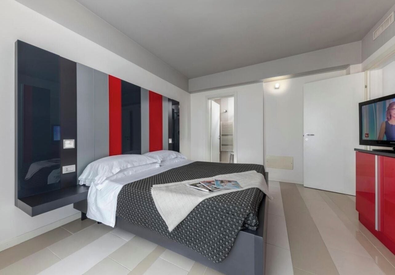A modern hotel room with a large bed, a TV, and a red cabinet.