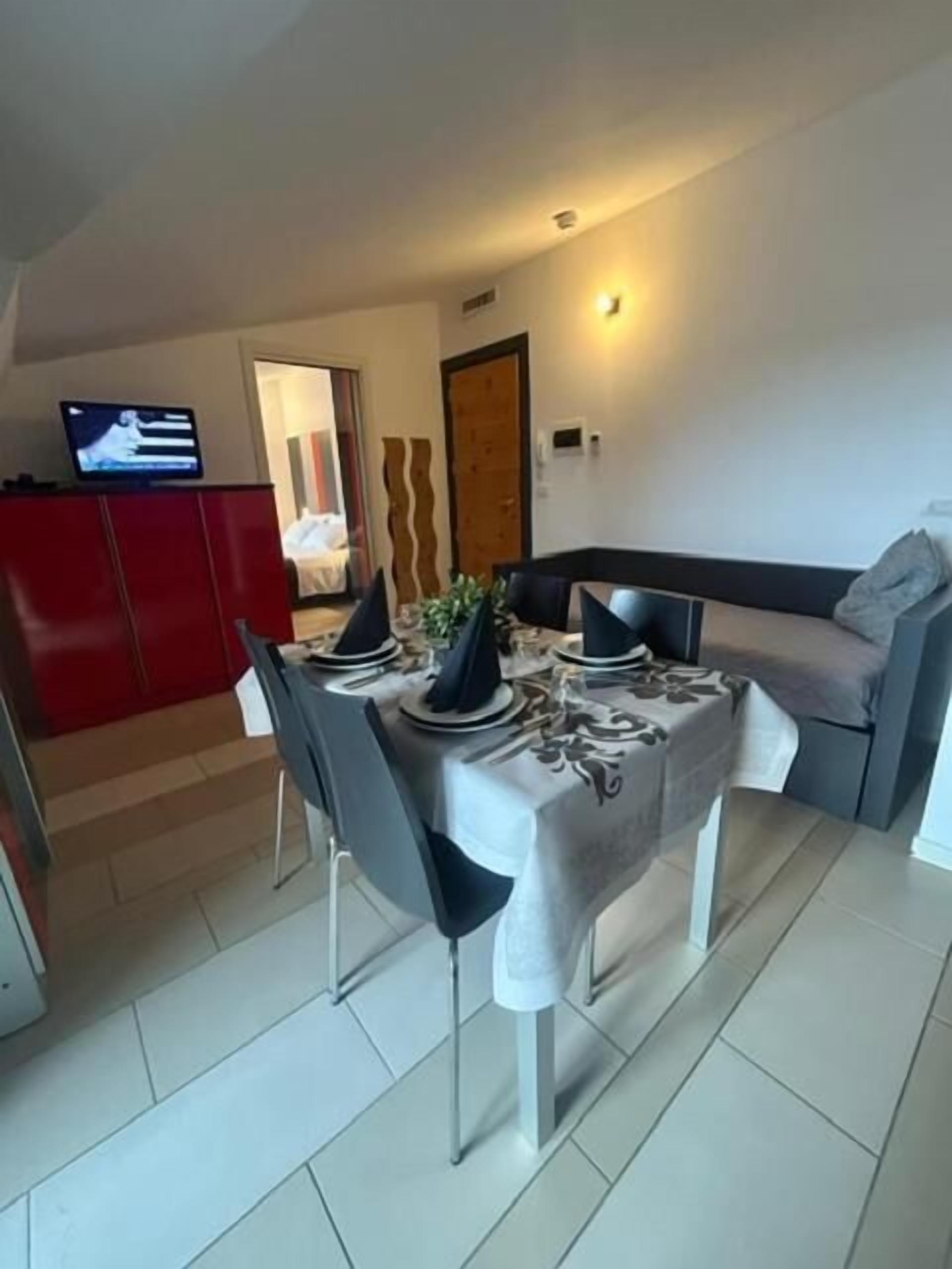 Un comedor con una mesa preparada para cuatro, un armario rojo y un televisor en la pared.
