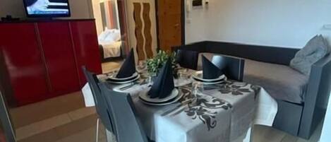 Un comedor con una mesa preparada para cuatro, un armario rojo y un televisor en la pared.