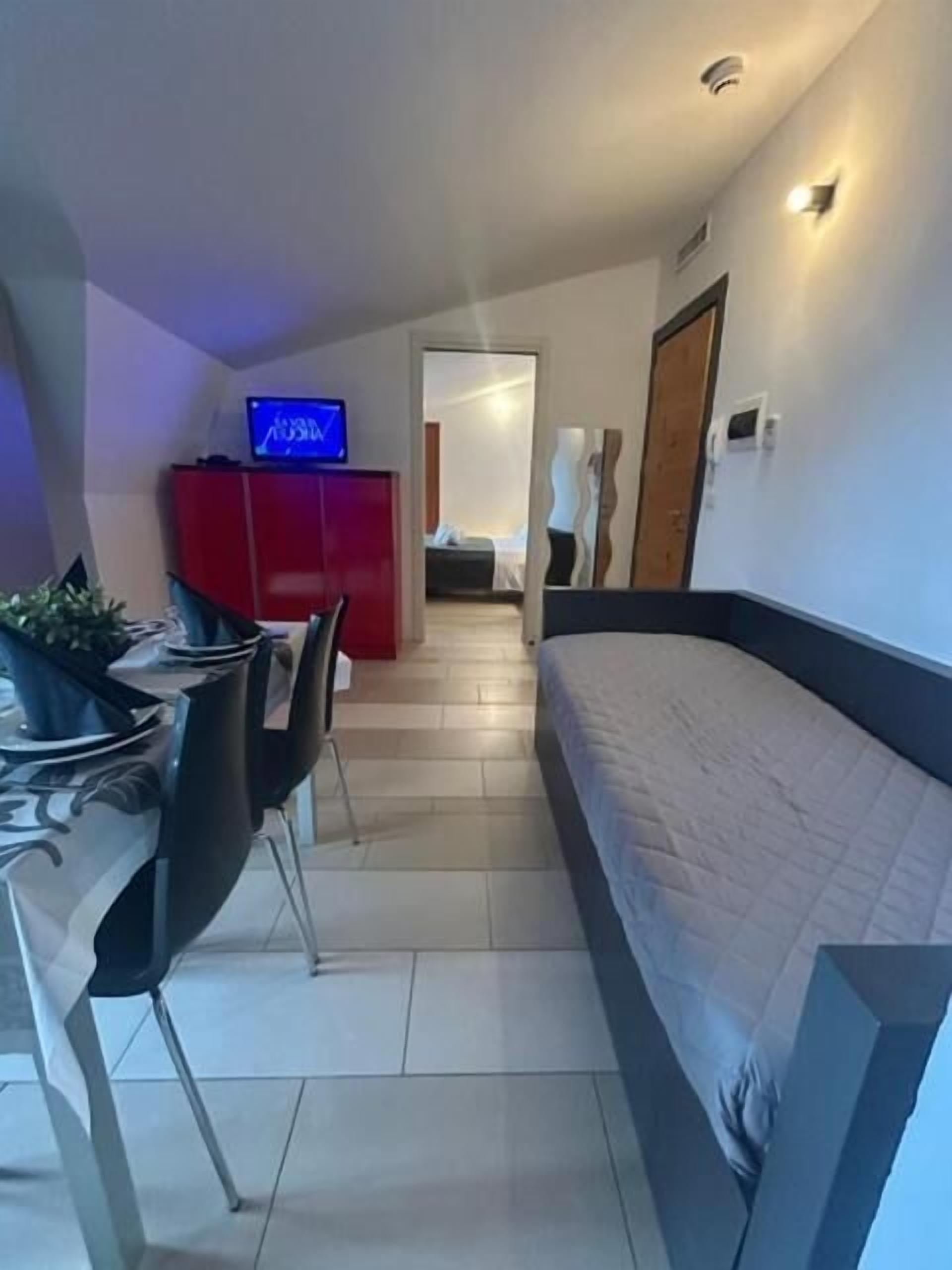 A modern hotel room with a bed, a TV, a dining area with chairs, and a red cabinet.