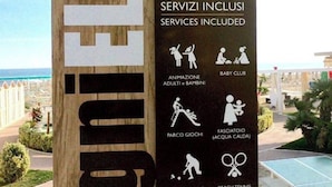 Schild für ein Hotel namens "Bagni 10" mit Annehmlichkeiten wie Babyclub, Animation für Erwachsene und Kinder, Spielbereich, Tennisplatz, Pool und WLAN.