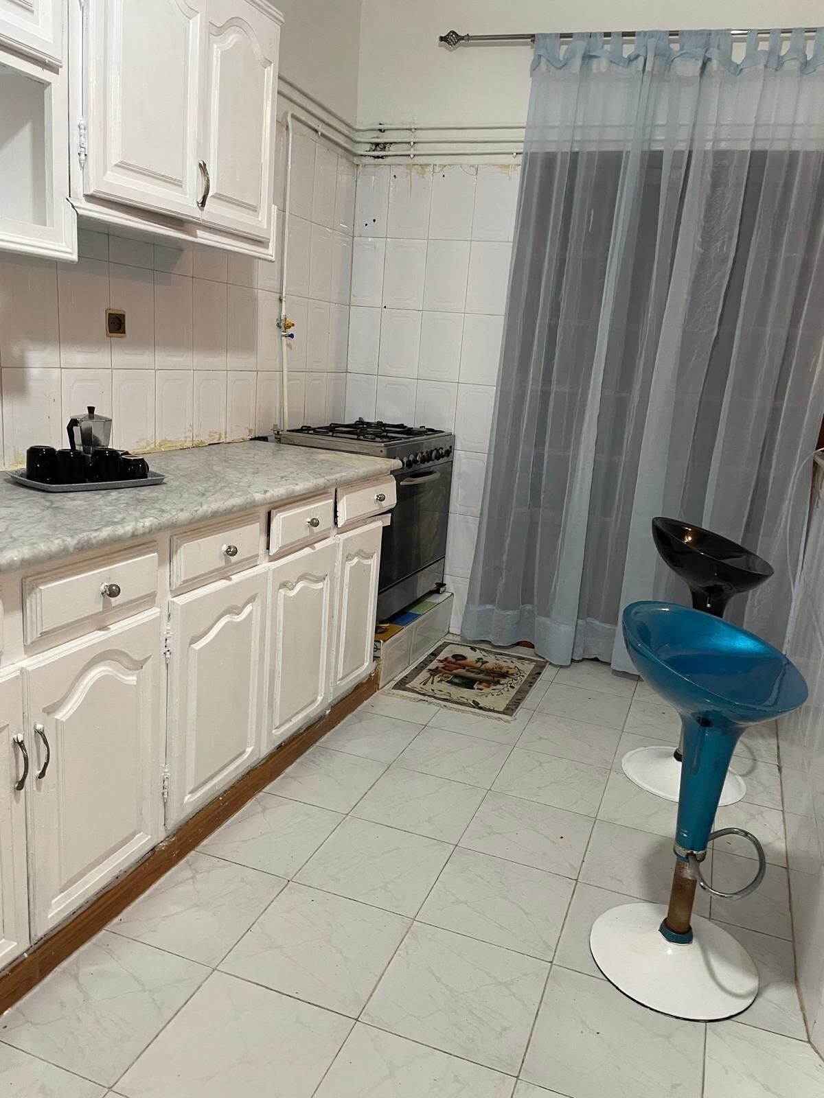 Una cocina con armarios blancos, estufa a gas, pileta y un taburete azul.