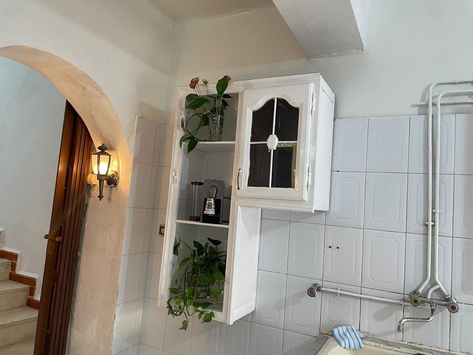 A bathroom with white tiled walls, a wooden door, a white cabinet with a window, and a towel rack.