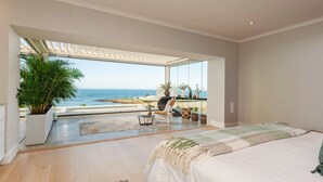 A bedroom with a large bed, a view of the ocean, and a seating area with a chair and a table. - Exclusive Ocean-View Villa, 200m from the Beach (Plettenberg Bay)