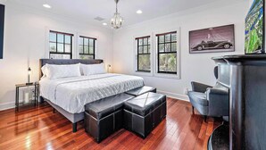 A bedroom with a bed, two windows, a chandelier, a painting, and a fireplace. - Palm Haven - Tropical Chic Home with Pool in Grandview Heights (West Palm Beach)