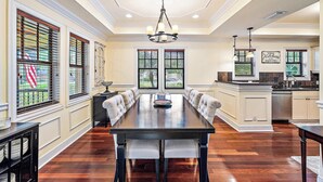 A spacious dining room with a long table, cushioned chairs, and a chandelier. - Palm Haven - Tropical Chic Home with Pool in Grandview Heights (West Palm Beach)