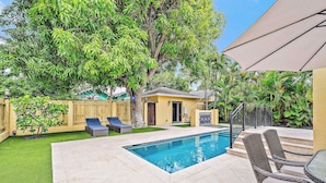 A swimming pool with a tiled deck, surrounded by a wooden fence, and a small tree. - Palm Haven - Tropical Chic Home with Pool in Grandview Heights (West Palm Beach)