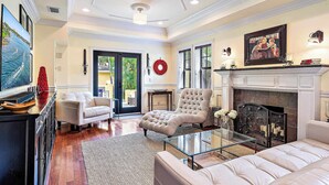 A spacious living room with a fireplace, a large window, and a comfortable seating area. - Palm Haven - Tropical Chic Home with Pool in Grandview Heights (West Palm Beach)