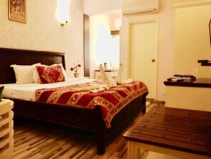 A hotel room with a bed, bedside table, and a wooden bench. - Hotel Glitz (Jaipur)