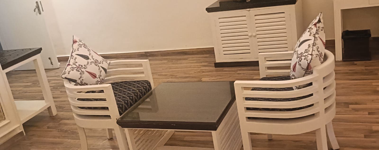 Un comedor con una mesa y cuatro sillas blancas, cada una con un cojín.