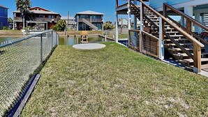 Un quartier résidentiel avec une pelouse verdoyante, un banc en bois, un petit étang et un escalier menant à une maison bleue.