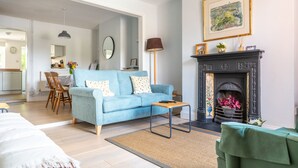 A living room with a blue sofa, a fireplace, and a dining area in the background. - Dragonfly Cottage, Holt, Norfolk (Holt)