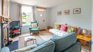 A living room with a sofa, armchair, TV, and a small table. - Dragonfly Cottage, Holt, Norfolk (Holt)