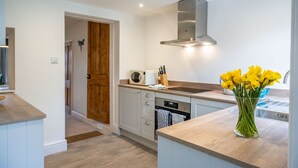 A modern kitchen with wooden cabinets, a stainless steel range hood, and a vase of yellow flowers on the countertop. - Dragonfly Cottage, Holt, Norfolk (Holt)