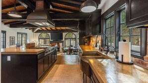 A modern kitchen with a central island, large windows, and a high ceiling with exposed beams.