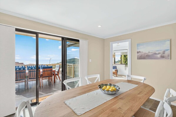 A dining area with a wooden table, white chairs, a bowl of lemons, and a view of the outdoors.
