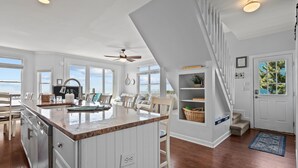 A spacious kitchen with a large island, white cabinetry, and a view to the outside. - Cassimir West | Stunning Oceanfront Duplex Retreat (Emerald Isle)