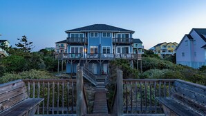 A multi-story house with a balcony, a wooden deck, and a staircase leading to the entrance. - Cassimir West | Stunning Oceanfront Duplex Retreat (Emerald Isle)