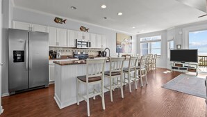 A modern kitchen with white cabinetry, stainless steel appliances, and a central island with seating. - Cassimir West | Stunning Oceanfront Duplex Retreat (Emerald Isle)