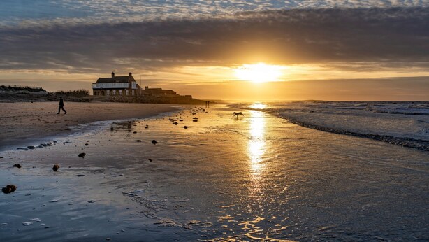 Ein Strand mit einem Gebäude und einem Sonnenuntergang.