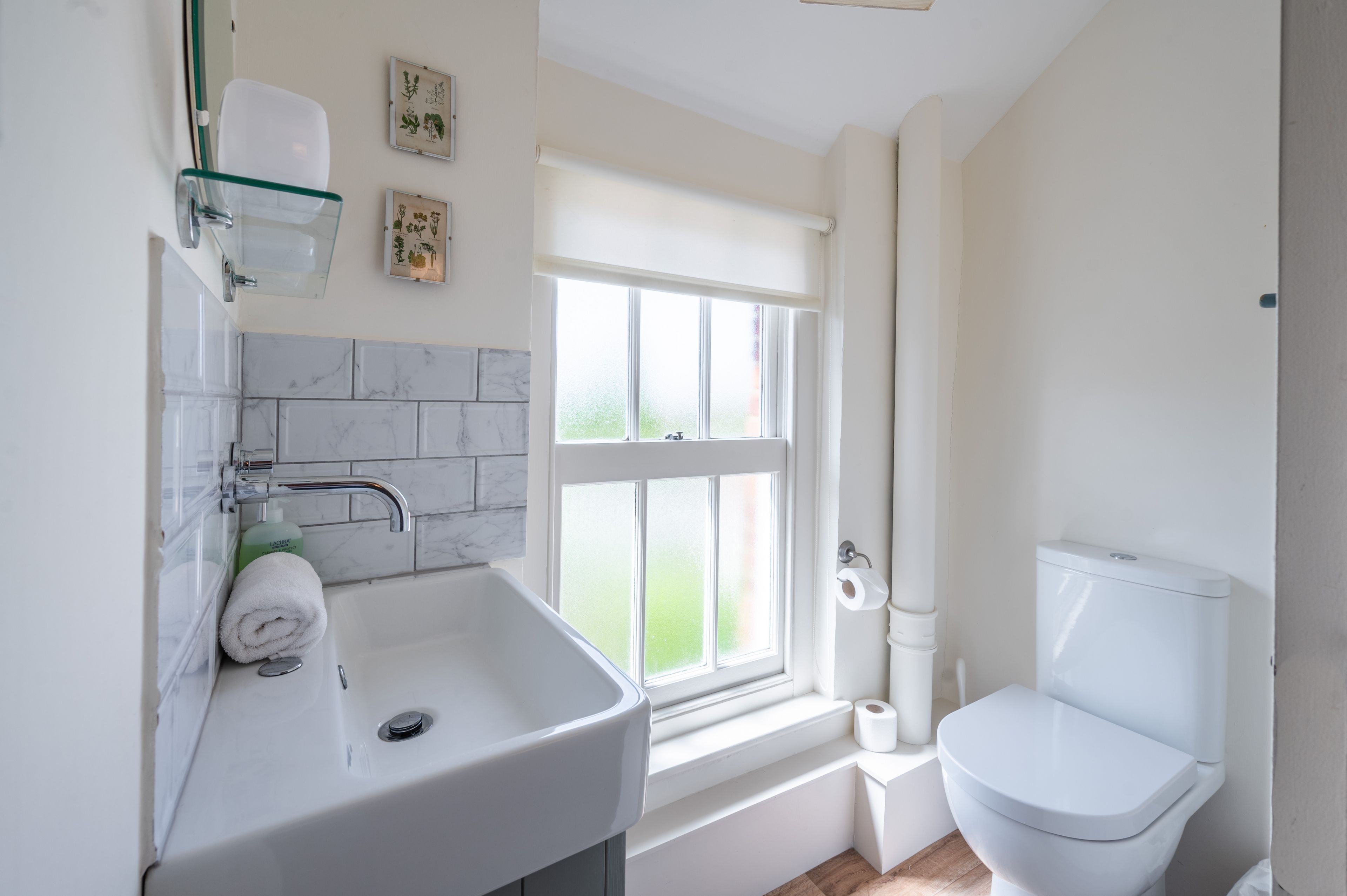 Un baño moderno con lavamanos, inodoro y ventana blancos.