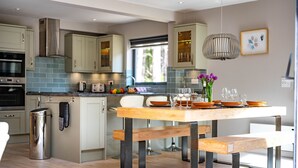 A modern kitchen with a wooden dining table, benches, and a hanging light fixture. - Liz's Lodge, Weybourne, Norfolk (Weybourne)