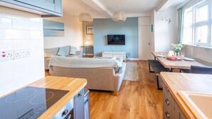 Una cocina moderna con estufa integrada, un comedor con mesa y sillas de madera, un sofá y un televisor montado en la pared.
