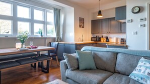 Una cocina moderna con armarios grises, un comedor con mesa y bancos de madera, y un sofá gris con una manta.