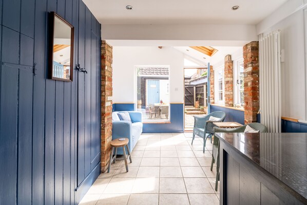 A modern interior with a blue door, a brick wall, a blue sofa, and a dining area with wicker chairs.