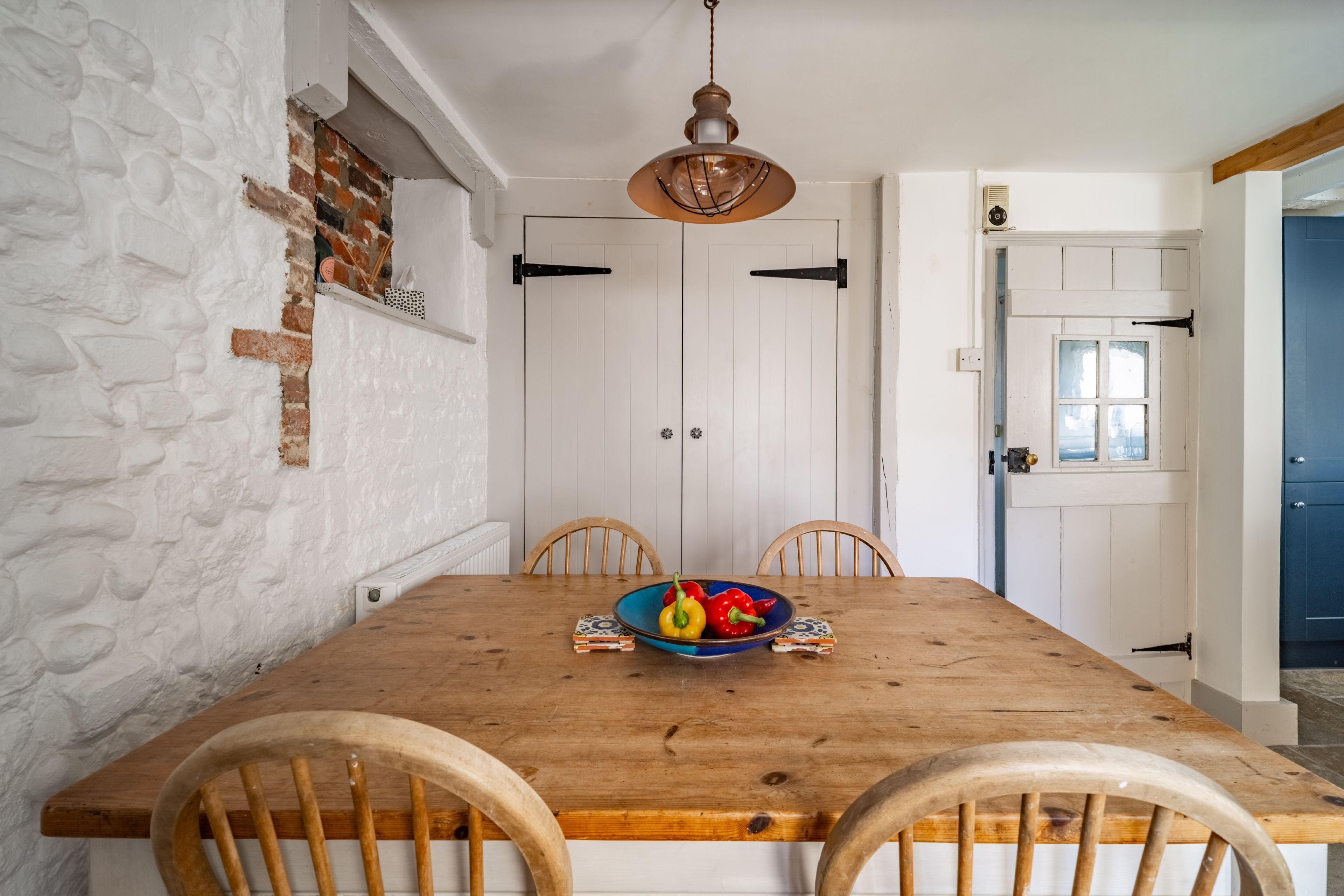 A dining area with a wooden table, four chairs, a bowl of fruit, and a hanging light fixture.