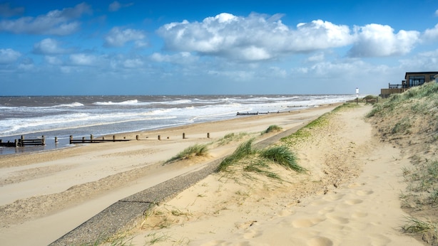 Une plage de sable avec une promenade en bois et un bâtiment visible au loin.