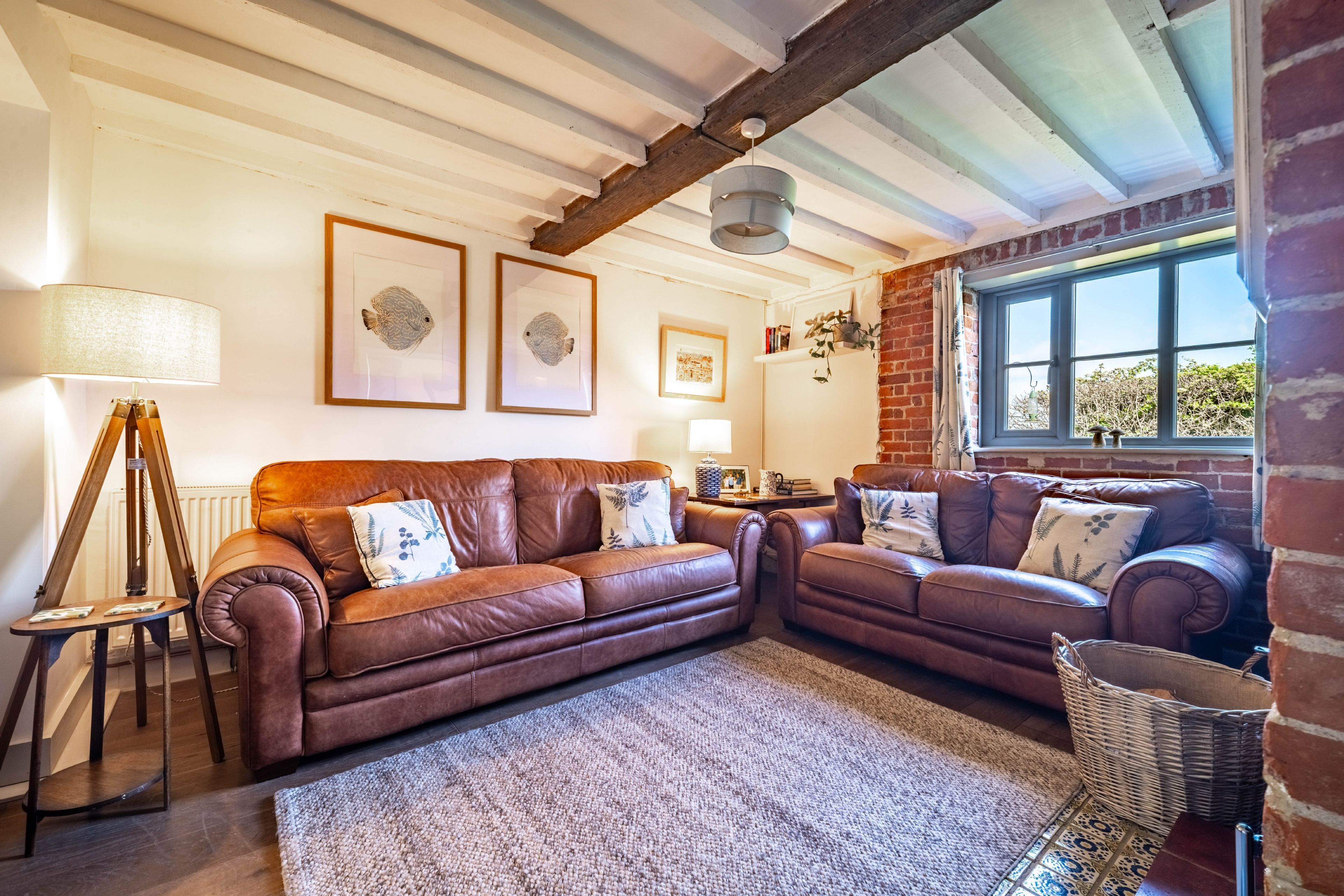 A cozy living room with two brown leather sofas, a patterned rug, and a large window with a view.