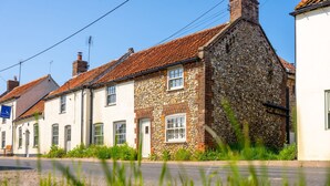 Une rangée de maisons traditionnelles en pierre et en briques, avec des toits en pente, une route pavée au premier plan et un ciel bleu dégagé.