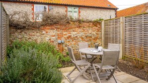 A patio with a round table and chairs, a stone wall, and a wooden fence.