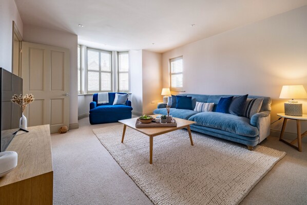 Una sala de estar moderna con un sofá azul, una mesa de centro de madera y un televisor sobre un mueble de madera.