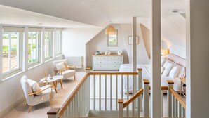 A spacious loft bedroom with a high ceiling, a wooden staircase, and a large window providing a view of the outdoors.